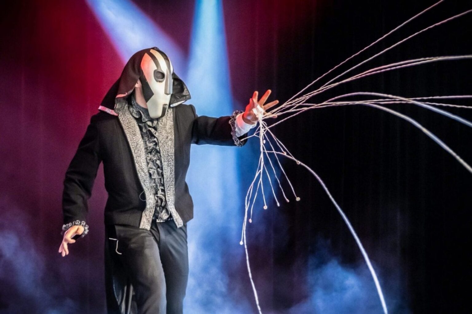 Daniel Kane i mask och mantel kastar ut vita serpentiner i rött och blått strålkastarljus